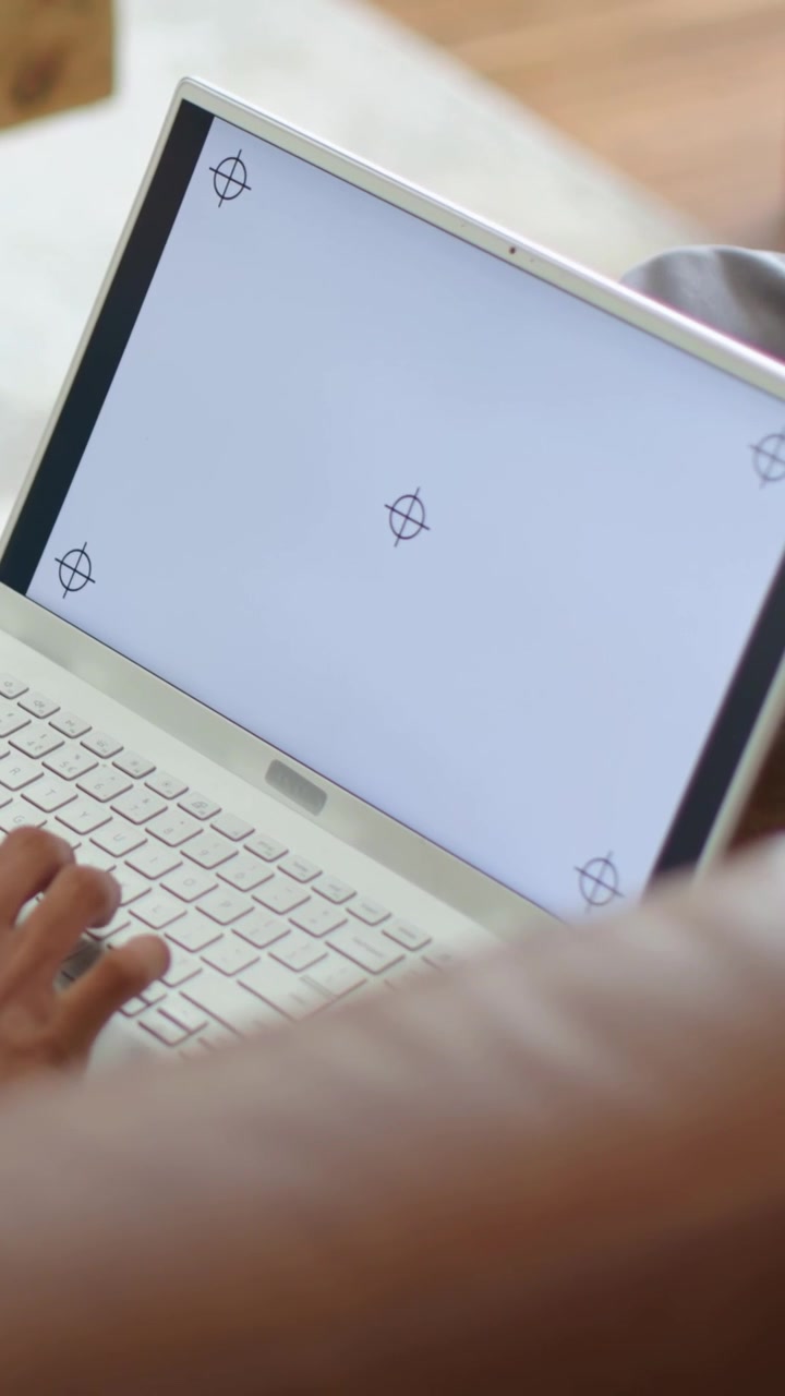 Vertical video: Camera shifting, man in gray pants typing on white laptop on couch with remote