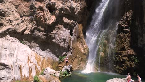 a man stands on rocks near a large waterfall with a pool of water below