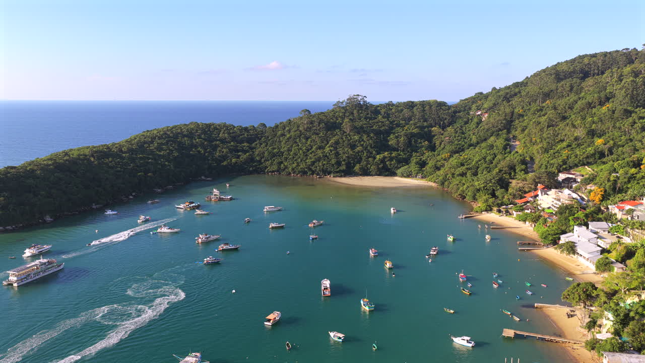 Barcos ancorados na praia da Caixa D'Aço, Porto Belo, Santa Catarina, Brasil, em uma baía abrigada delimitada por vegetação da Mata Atlântica e uma enseada de areia sob condições claras, tomada de revelação com recuo de drone.