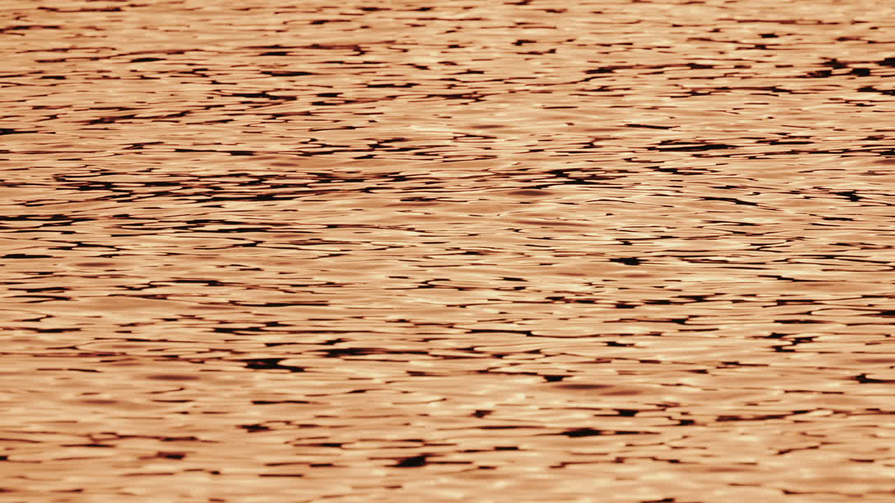 Close up of orange and gold sunset reflections moving across gentle water ripples