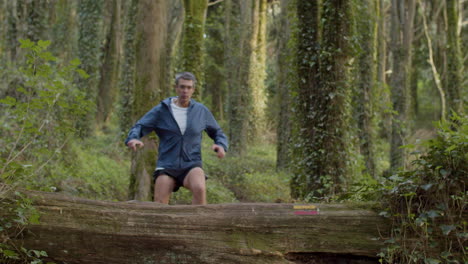 focused man running and jumping over logs in forest