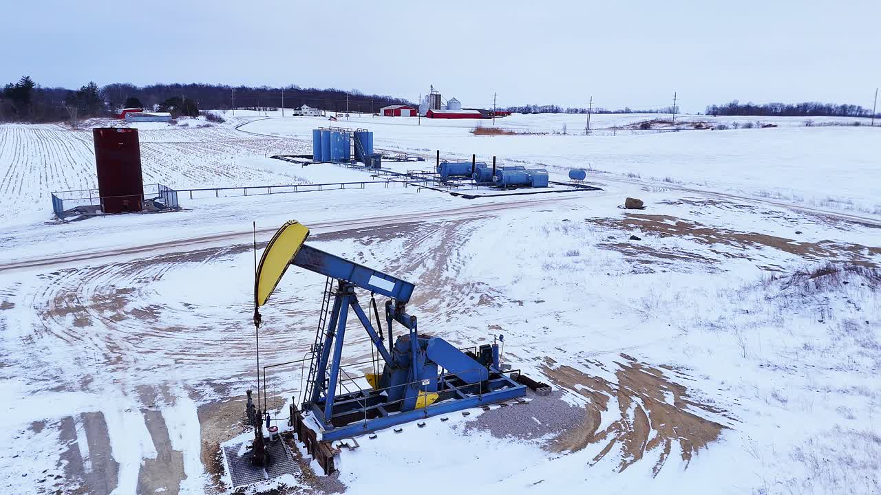 Pumpjack operating in a winter field, representing energy production and fossil fuels, southeast Michigan, USA in aerial view