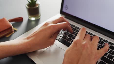 Hands-typing-on-laptop-keyboard,-with-plant-and-purse-on-desk