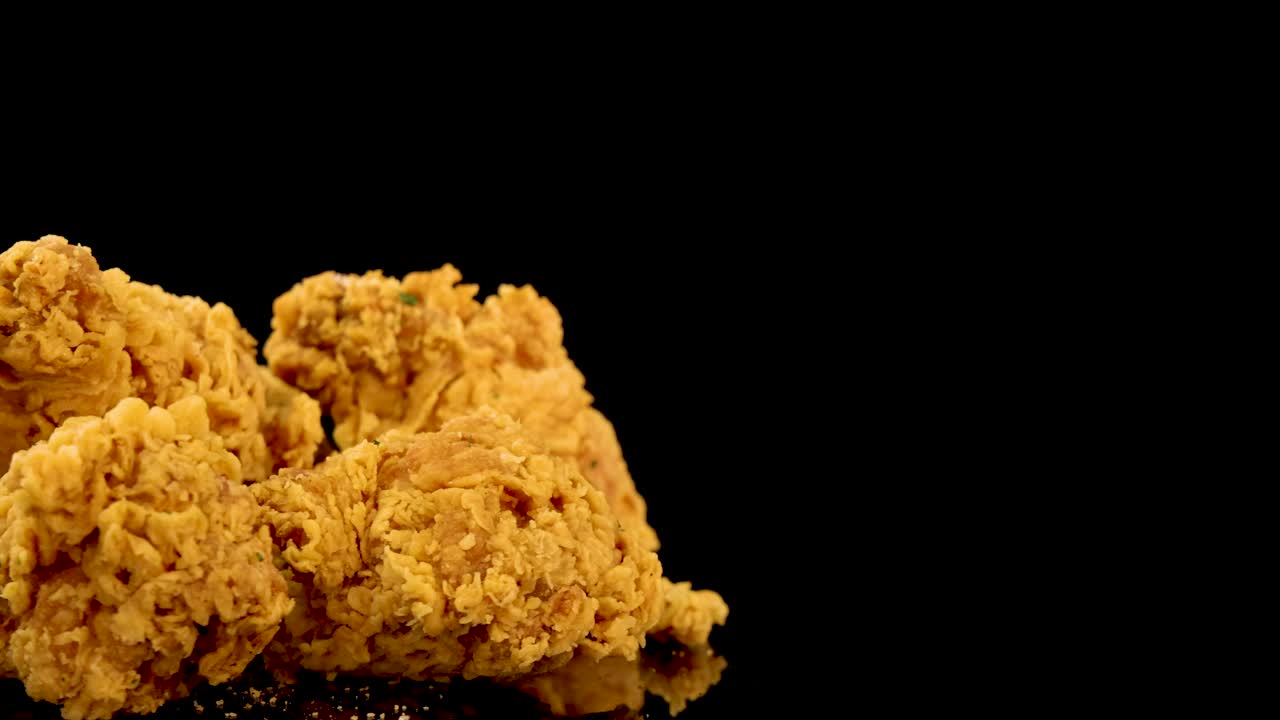 Golden, crumbed chicken breasts and thighs rotate and zoom in slow motion against a black background, highlighting texture and crunchy coating under studio lighting