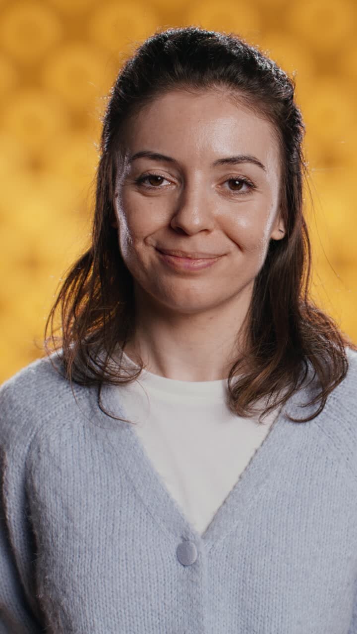 Giovane donna felice sorridente che saluta su sfondo giallo