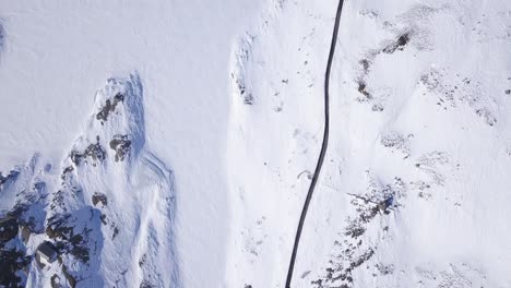 Langsam-Nach-Oben-Geneigte-Drohnenluftaufnahme-Von-Schneebedeckten-Bergen,-Die-Einer-Kurvenreichen-Straße-Folgen,-Gefrorener-See,-Der-Mit-Schnee-Bedeckt-Ist