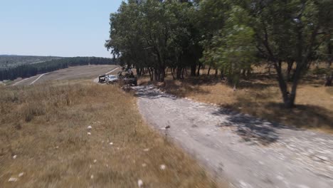 Israel-Army-squad-soldiers-on-vehicles-driving-through-green-field-at-training-ground-country-road,-Aerial-Tracking-shot