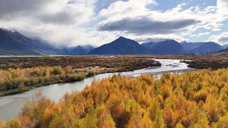 aerial view of vibrant autumn foliage along a winding river under dynamic skies in glenorchy, new zealand