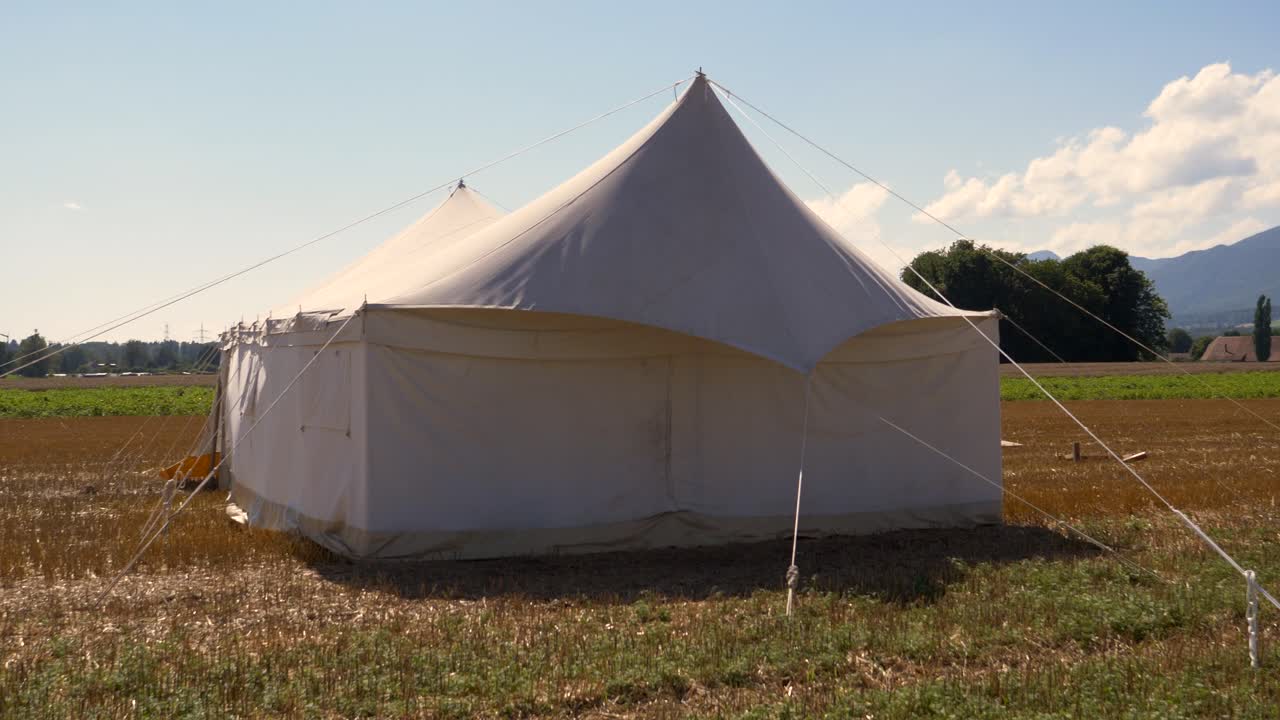 Static shot of large tent build on agricultural field during sunny day - Beautiful mountains in background