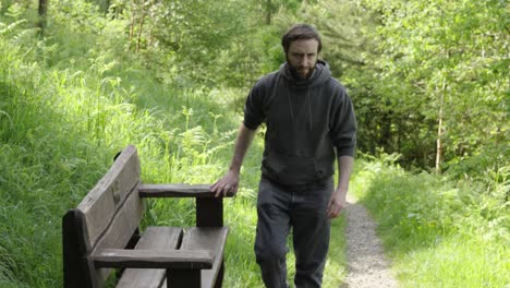 young man sitting down on bench on forest trail walk to rest and take in view