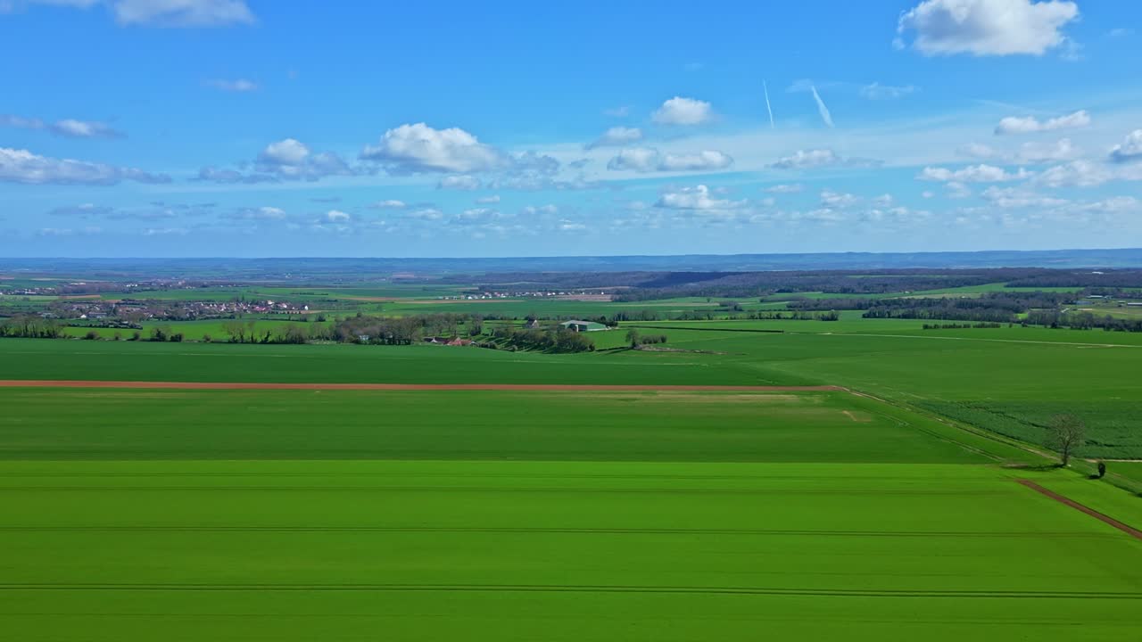 Lush green agricultural fields in rural France during spring, cultivation, arable land, and distant village under blue sky, vibrant and vivid colors, copy space. Aerial forward