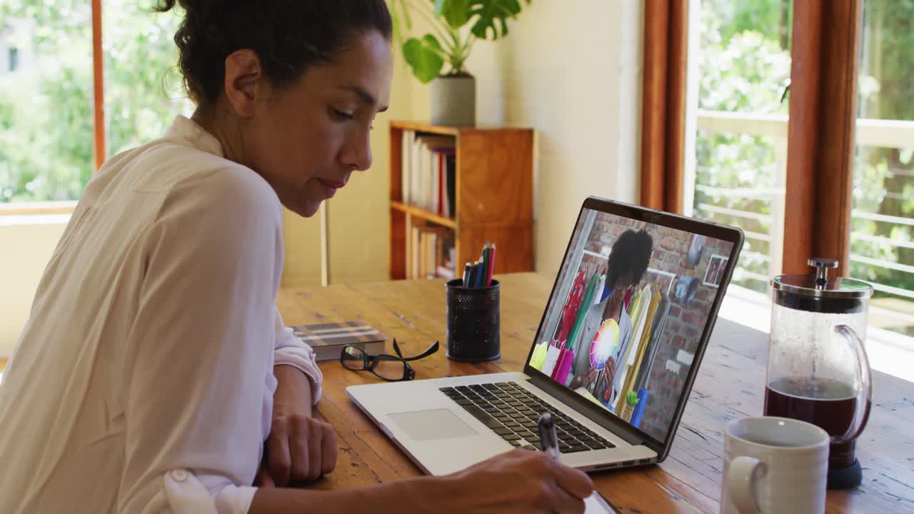 Eine afrikanisch-amerikanische Frau macht Notizen, während sie zu Hause einen Videoanruf am Laptop führt.