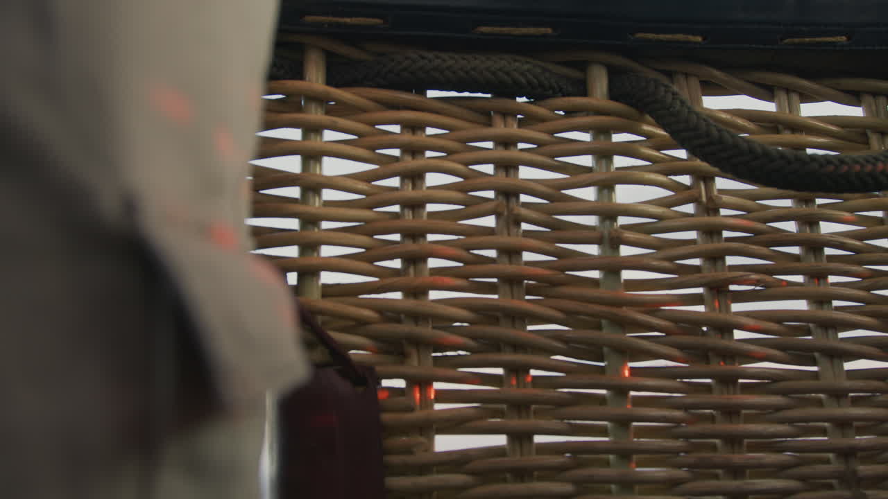 close up of intricate wicker basket wall illuminated by warm sunset glow with braided rope detail and metal fittings framing air balloon interior texture in golden light under pastel sky