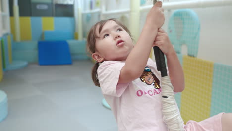 happy 4 year old blond girl riding zip line in slow motion sitted holding rope inside the playroom