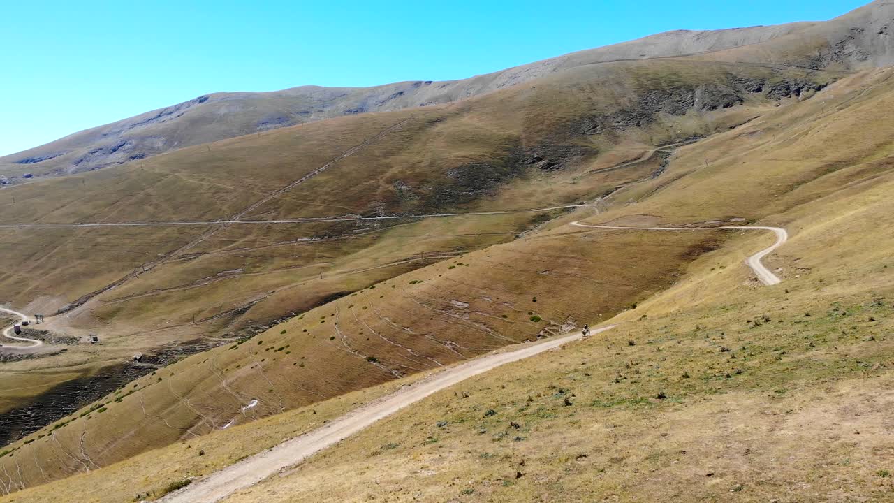공중:푸른 하늘 아래 여름에 높은 산의 황량한 지역에서 내리막길을 가는 산악 자전거 타는 사람