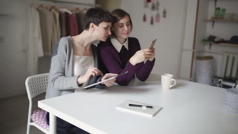 Zwei-Junge-Frauen-Nutzen-Tablet-PC-Und-Mobiltelefon-Zum-Online-Einkauf
