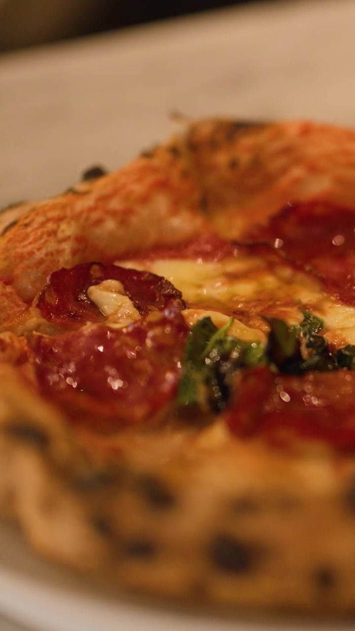 Scatto macro di una pizza al salame piccante con impasto a lievitazione naturale e crosta carbonizzata su un tavolo di marmo in un ristorante.