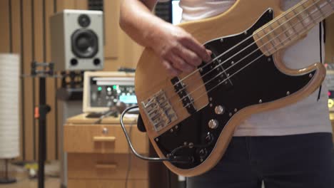 closeup of bass guitar player playing in recording studio, blurry background