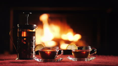 A-Teapot-And-Two-Glass-Cups-With-Tea-Stand-On-A-Table-Against-The-Background-Of-The-Fireplace-Where-