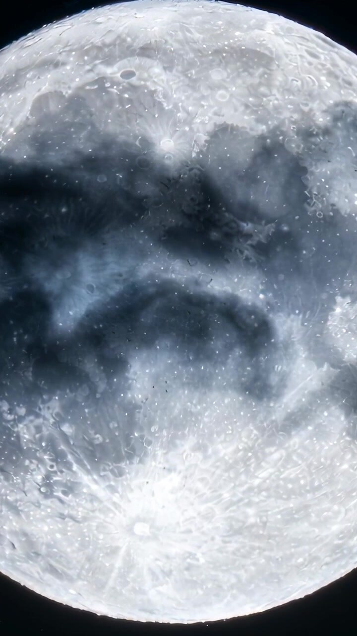 Vídeo vertical: Nuvens impulsionadas pelo vento passando, obscurecendo crateras da lua quase cheia no céu noturno escuro.