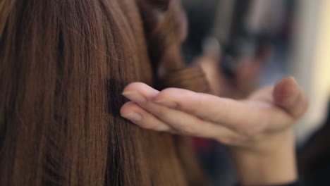el peluquero continúa rizando el cabello a una hermosa chica de cabello largo con una estratagema.