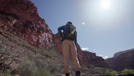 fotógrafo mira a su alrededor mientras sostiene su cámara en el gran cañón en una caminata soleada por la tarde