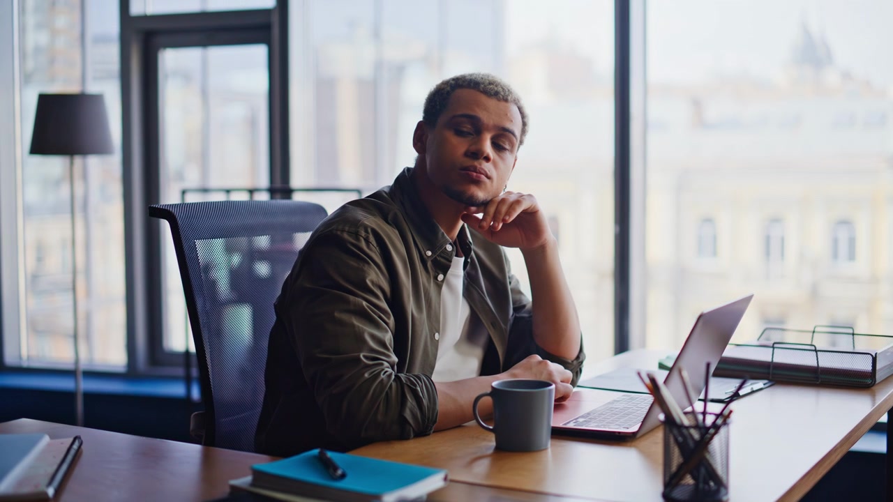 Thoughtful man taking off glasses at office desk. Pensive freelancer thinking