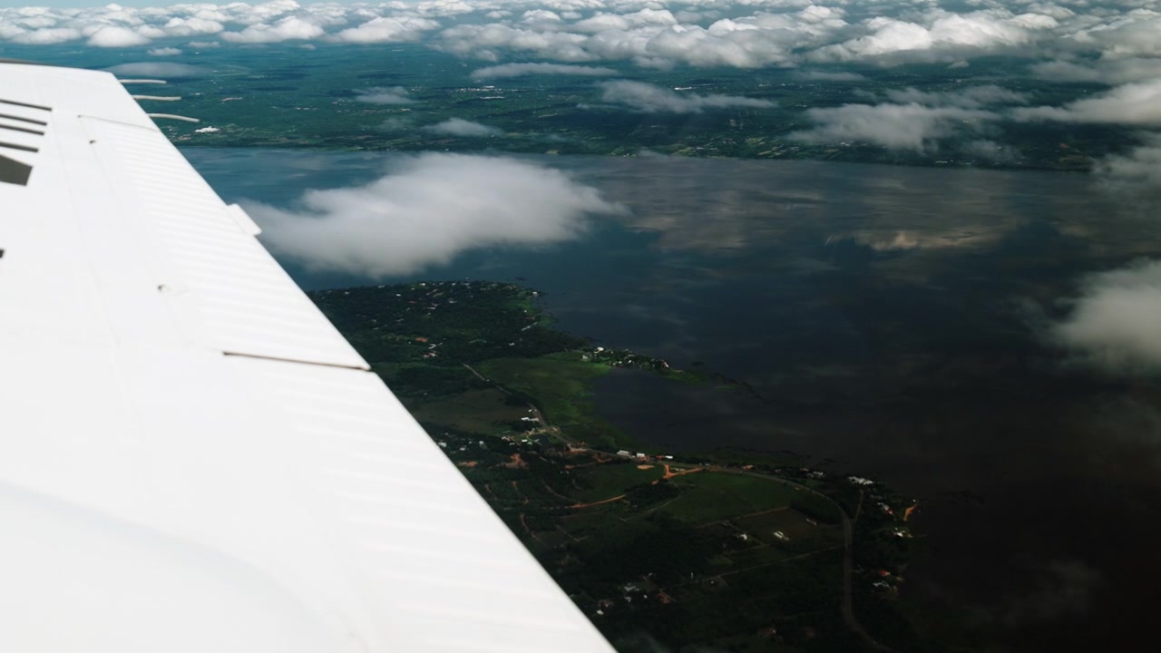 Udsigt fra et flyvindue over Paraguay, der viser vinge, flod og grønt landskab med spredte skyer. Indfanger perspektivet af flyrejser og Sydamerikas naturskønhed.