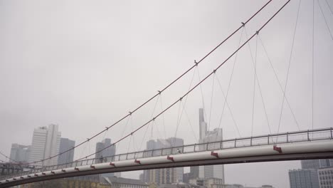 Eine-Fußgängerbrücke-Mit-Einem-Vogel-Mit-Blick-Auf-Die-Frankfurter-Skyline-An-Einem-Bewölkten-Tag