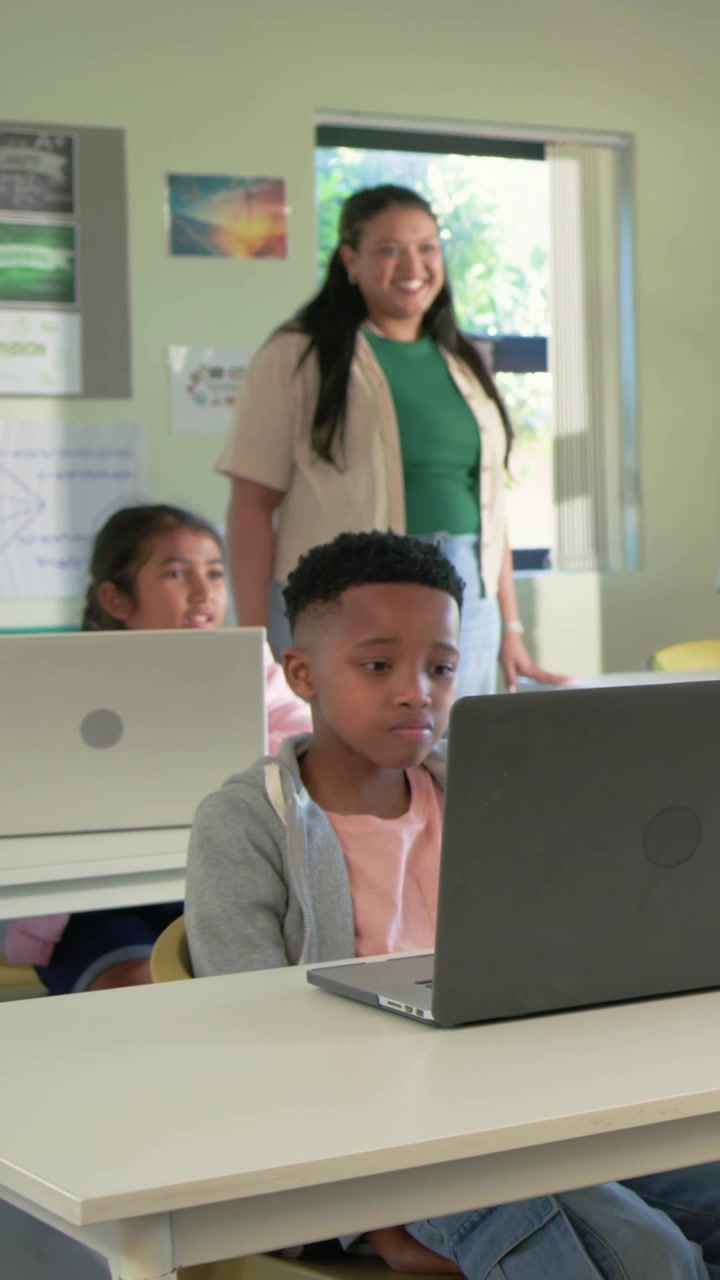 Video verticale: Rispondendo all'indicazione dell'insegnante, un alunno in prima fila sposta lo sguardo e digita sul laptop in classe.