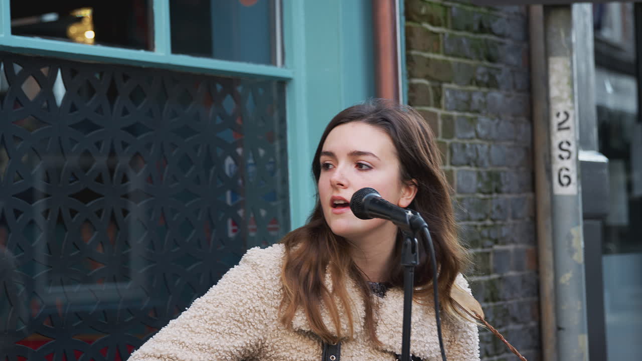여자 음악가 는 거리 에서 야외 에 있는 군중 들 에게 노래 를 부르고 어쿠스틱 기타 를 연주 하고 있다