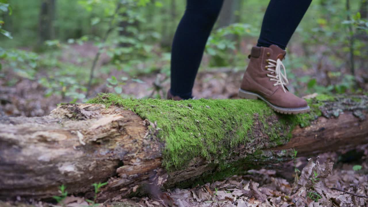 Close-up view of a hiker’s boots stepping over a moss-covered log in the forest. The scene captures the essence of adventure and nature exploration, highlighting textures of moss and woods