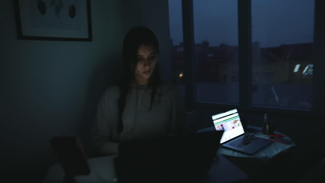 Woman working on a laptop in a dark room at night
