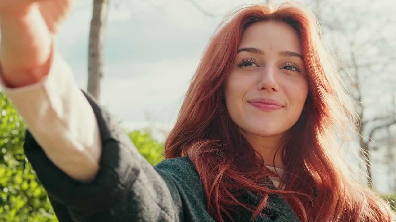 Giovane donna felice con i capelli rossi che si scatta un selfie all'aperto.