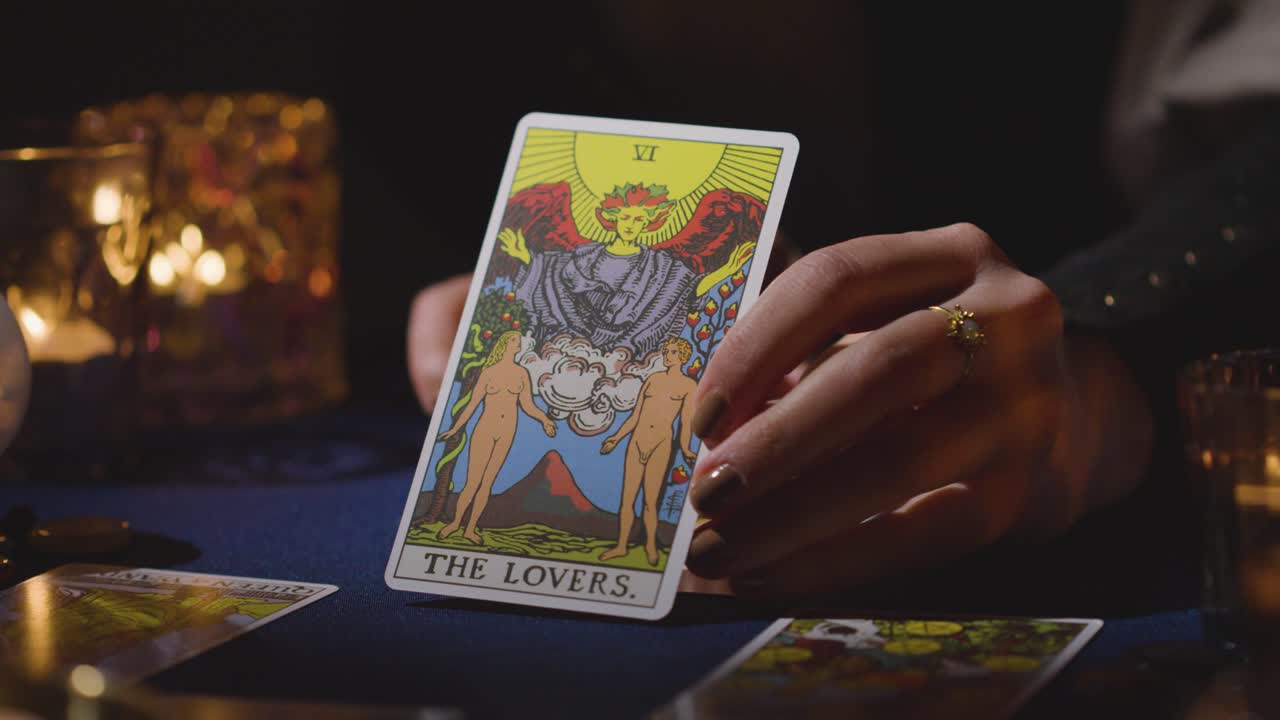 primer plano de una mujer dando una lectura de cartas del tarot en una mesa a la luz de las velas sosteniendo la carta de los amantes 3