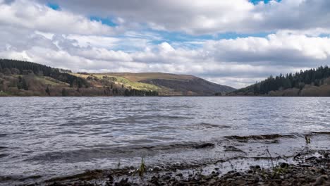 Timelapse-De-4k-En-El-Borde-Del-Agua-Mientras-Las-Nubes-Cruzan-El-Cielo-Y-Sobre-Las-Colinas-En-El-Embalse-De-Llwyn-on,-Brecon-Beacons,-Sur-De-Gales,-Reino-Unido