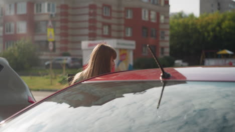 young female driver with long hair gets into red automobile