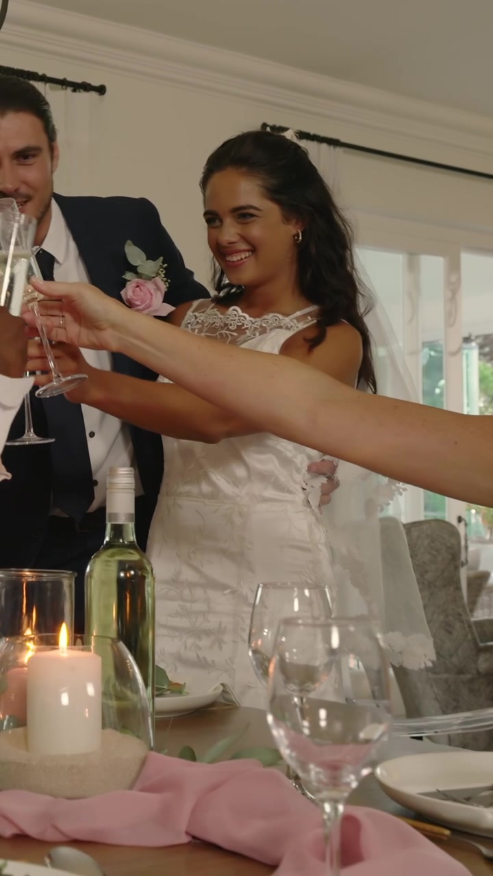 Vertical video: Newlywed couple in dress and suit rising at table, raising flutes after guest toast