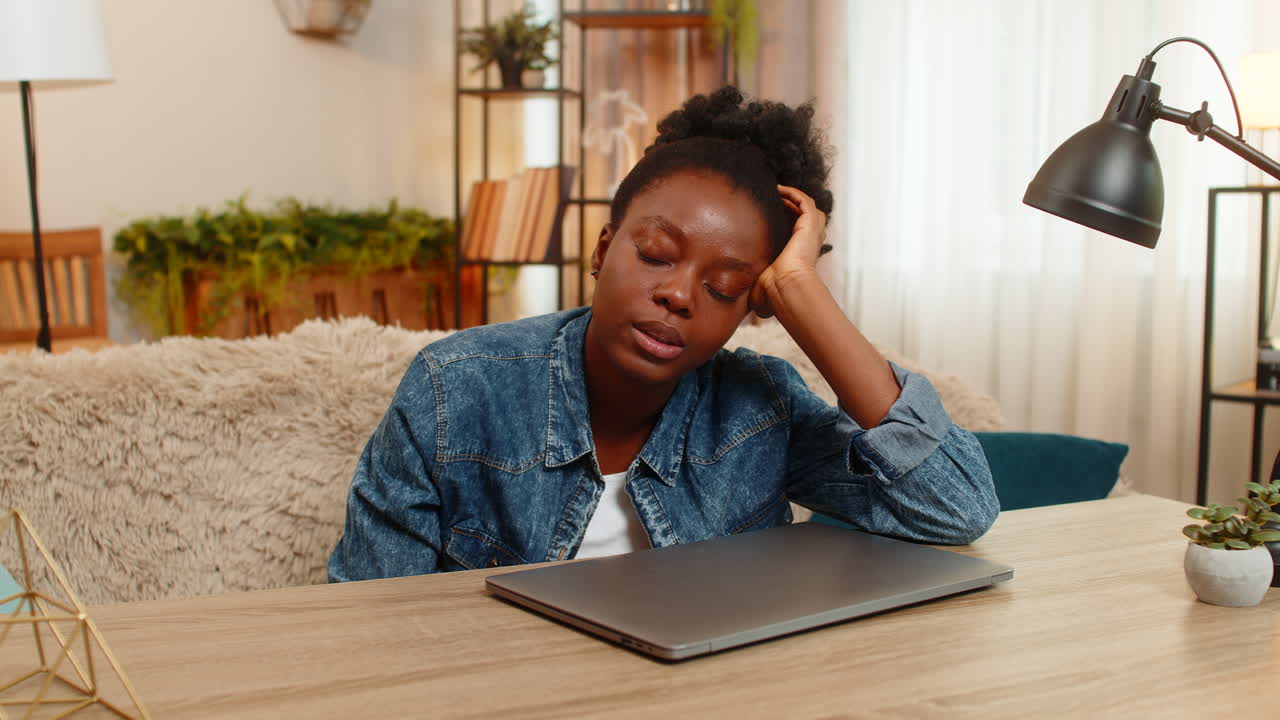 Afroamerikansk ung kvinne lukker laptop stresset etter en lang dag med online læring ved bordet hjemme