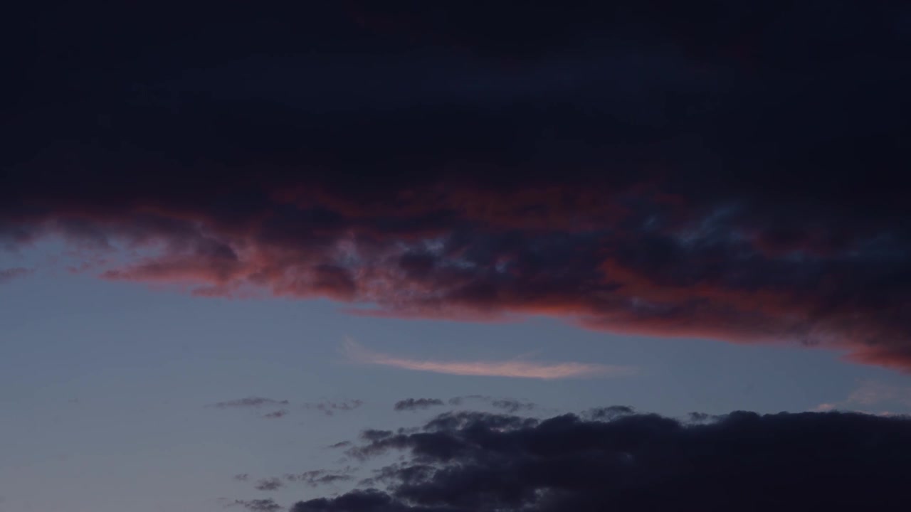 High angle view panning across dramatic clouds illuminated with red and orange sunset glows, creating layered formations against a deep blue evening sky.