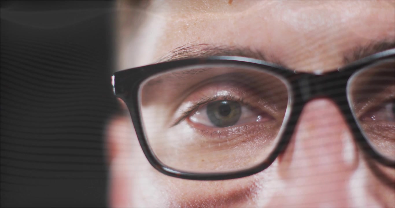 Homem usando óculos pretos mostrando close-up do olho enquanto ondas flutuam criando sombras para tecnologia.