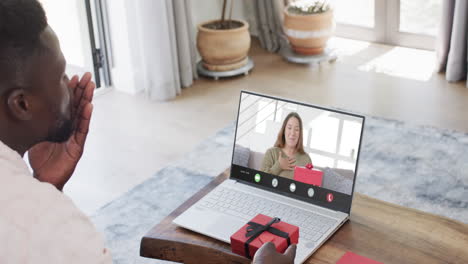 African-american-man-holding-gift-and-talking-with-caucasian-woman-on-laptop-screen