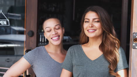 Portrait-Of-Two-Female-Owners-Of-Start-Up-Coffee-Shop-Or-Restaurant-Standing-In-Doorway