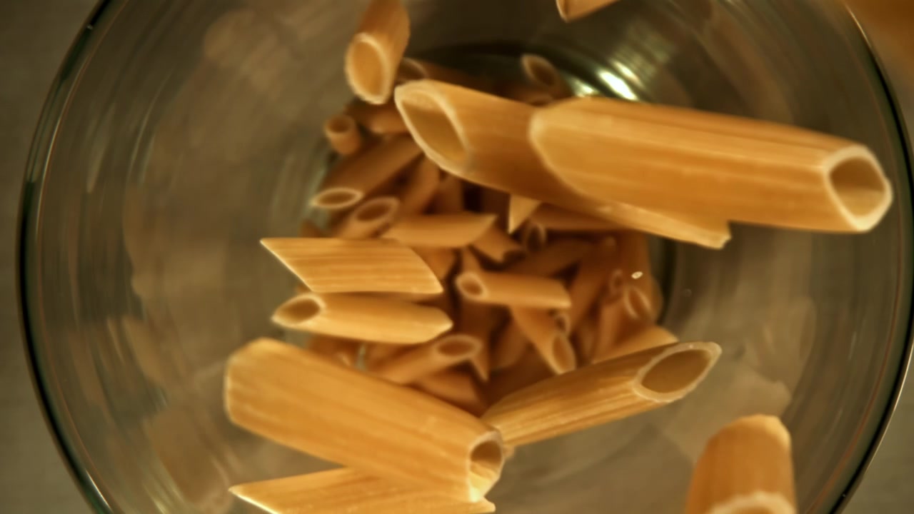 Penne che cadono al rallentatore in una ciotola di vetro