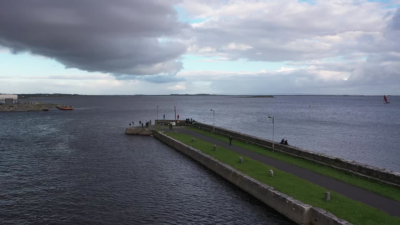 съемка с беспилотника, движущегося вперед, запечатлела пирс ниммо в галвее в пасмурный день с облачным небом, придающим драматизм