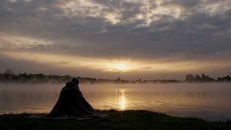 person sitting by a misty lake at sunrise