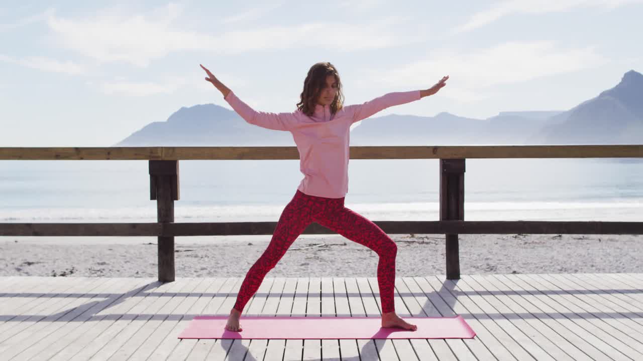Donna multietnica in salute che pratica yoga all'aperto, in piedi e che si allunga in riva al mare.