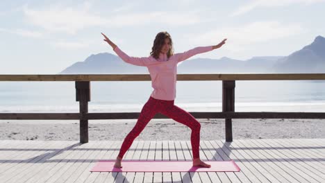 Healthy-mixed-race-woman-practicing-yoga-outdoors,-standing-and-stretching-by-the-sea