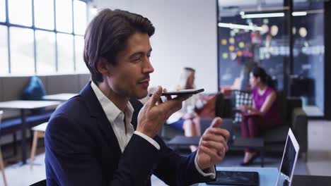 Caucasian-businessman-sitting-talking-on-smartphone-in-office-with-coworkers-in-background