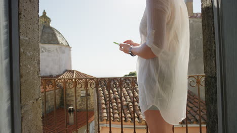 young woman using smartphone browsing online sending text messages enjoying sharing summer vacation experience relaxing on balcony in rustic villa